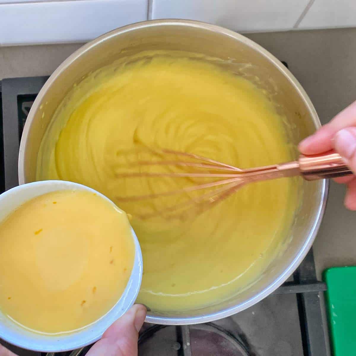 Egg yolk being poured into a pot of custard being mixed on the stovetop.