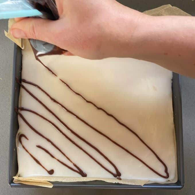 Melted milk chocolate being poured over the white icing to make custard squares.