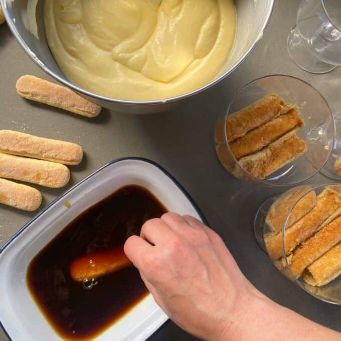 One sponge finger being dipped into the coffee liqueur for just a second the arranged into the individual glasses