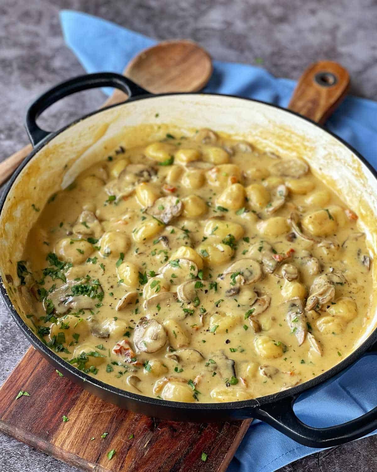 Cooked Mushroom Gnocchi in a round ceramic dish, sitting on a wooden chopping board. Scatted parsley over the top.