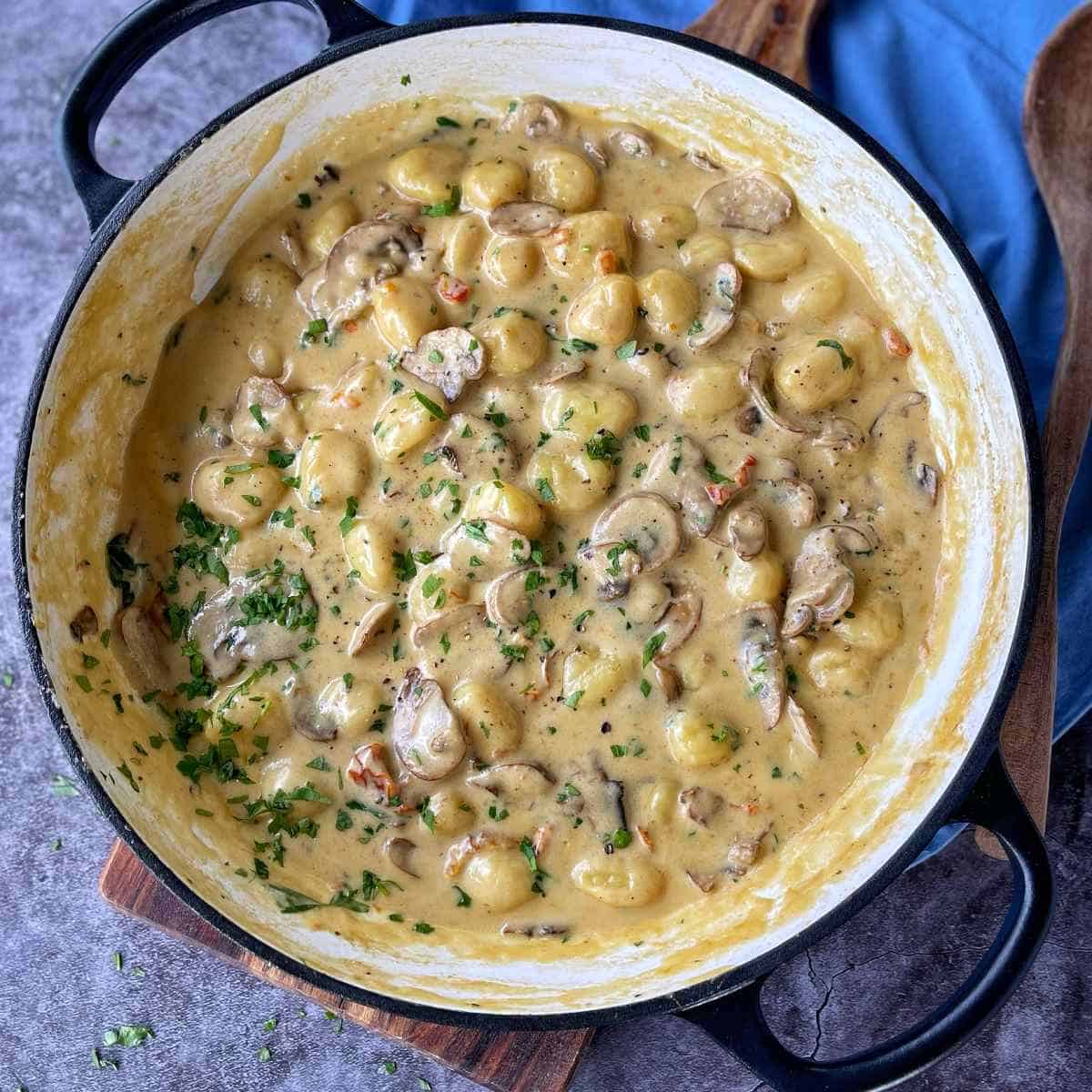 Cooked Mushroom Gnocchi in a round ceramic dish, sitting on a wooden chopping board. Scatted parsley over the top.