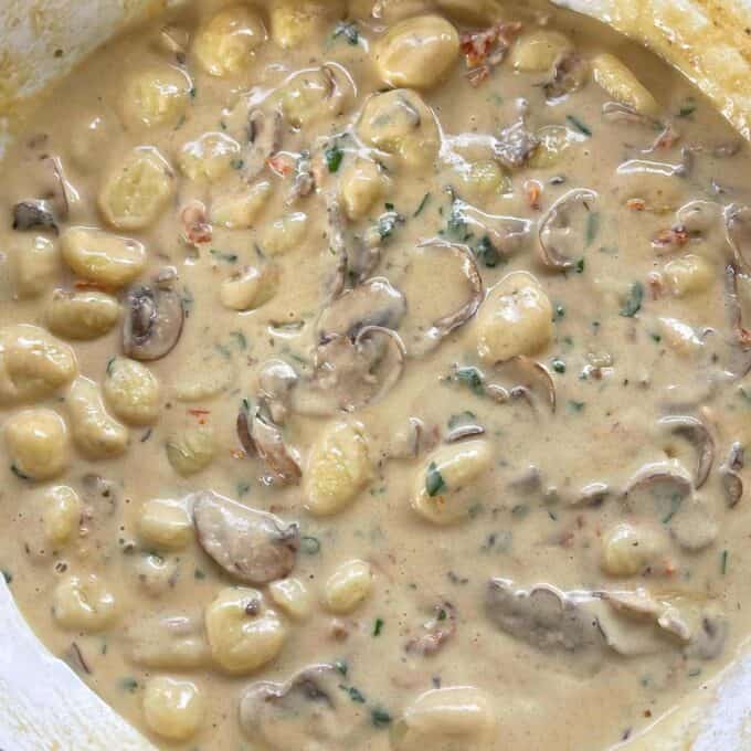 Mushroom Gnocchi simmering in a round ceramic dish over a medium heat