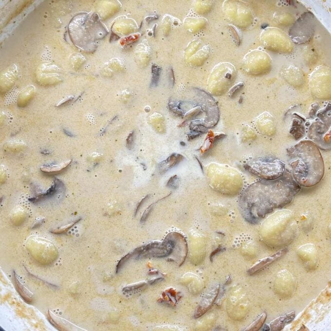 Mushroom Gnocchi simmering in a round ceramic dish over a medium heat