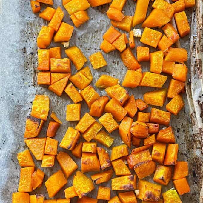 Cooked peices of cubed pumpkin on a lined baking tray.