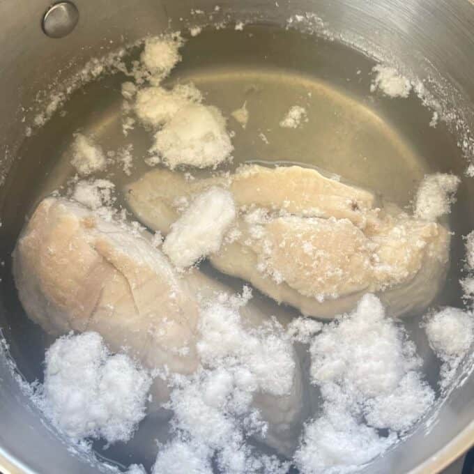 Two chicken breasts poaching in a small pot