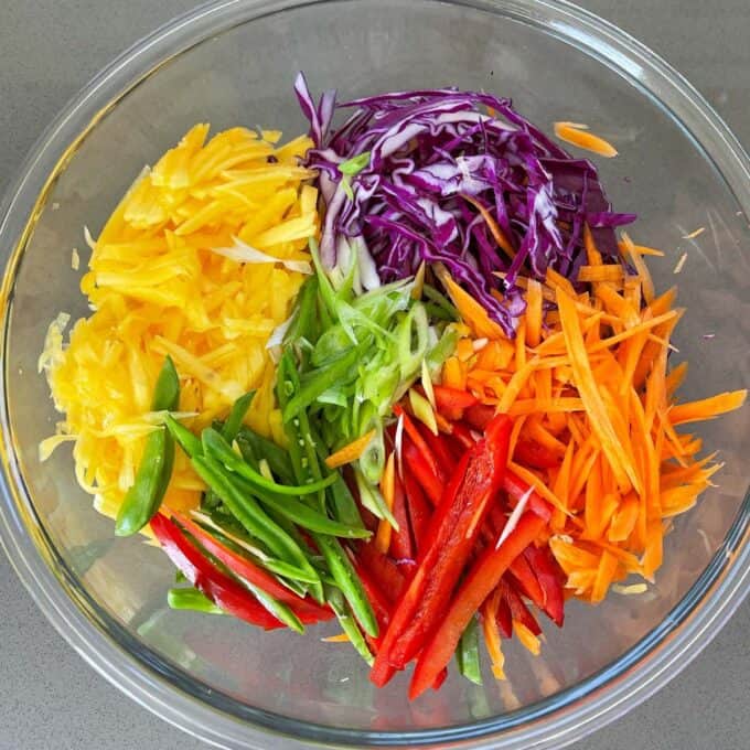 A glass bowl filled with the slaw vegeteables all sliced for Thai Style Chicken Slaw