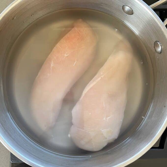 Two chicken breasts poaching in a small pot