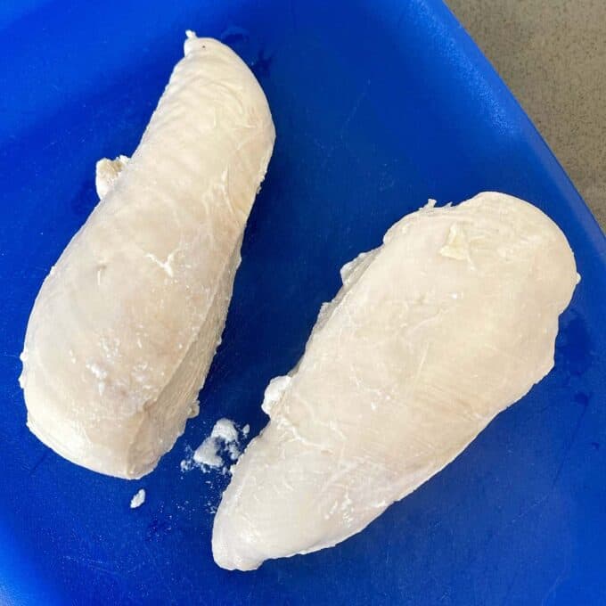 Two poached chicken breasts sitting on a blue chopping board.