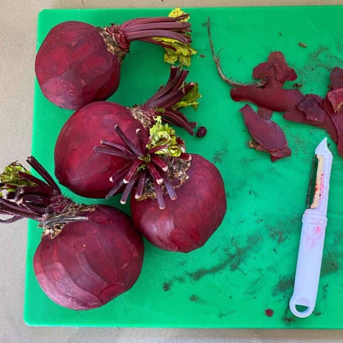 Four pealed beetroot on a green chopping board