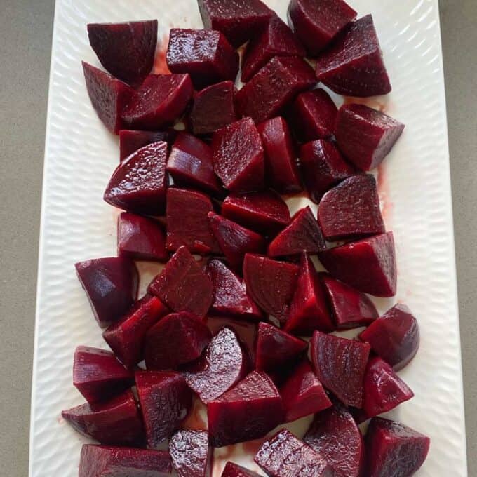 Cooked and cooled roasted beetroot with balsamic glaze on a long white platter.