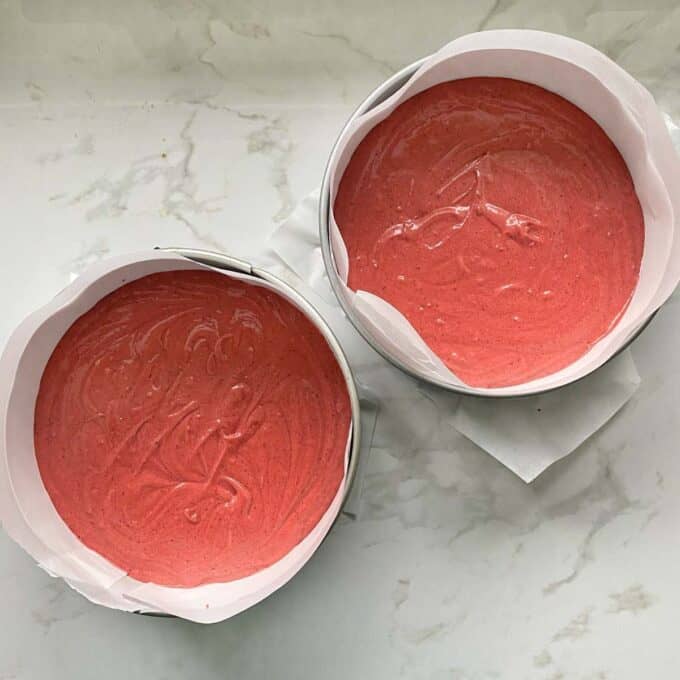 Two lined round cake tins filled with Red Valvet Cake batter sitting on a marbel bench top