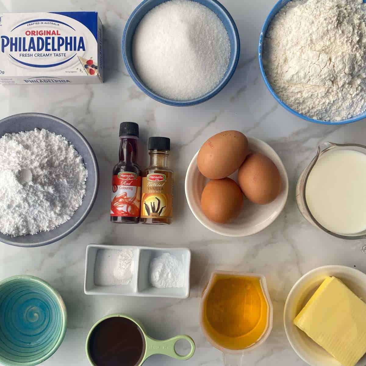 The ingredients to make Red Valvet Cake on a marbel bench top