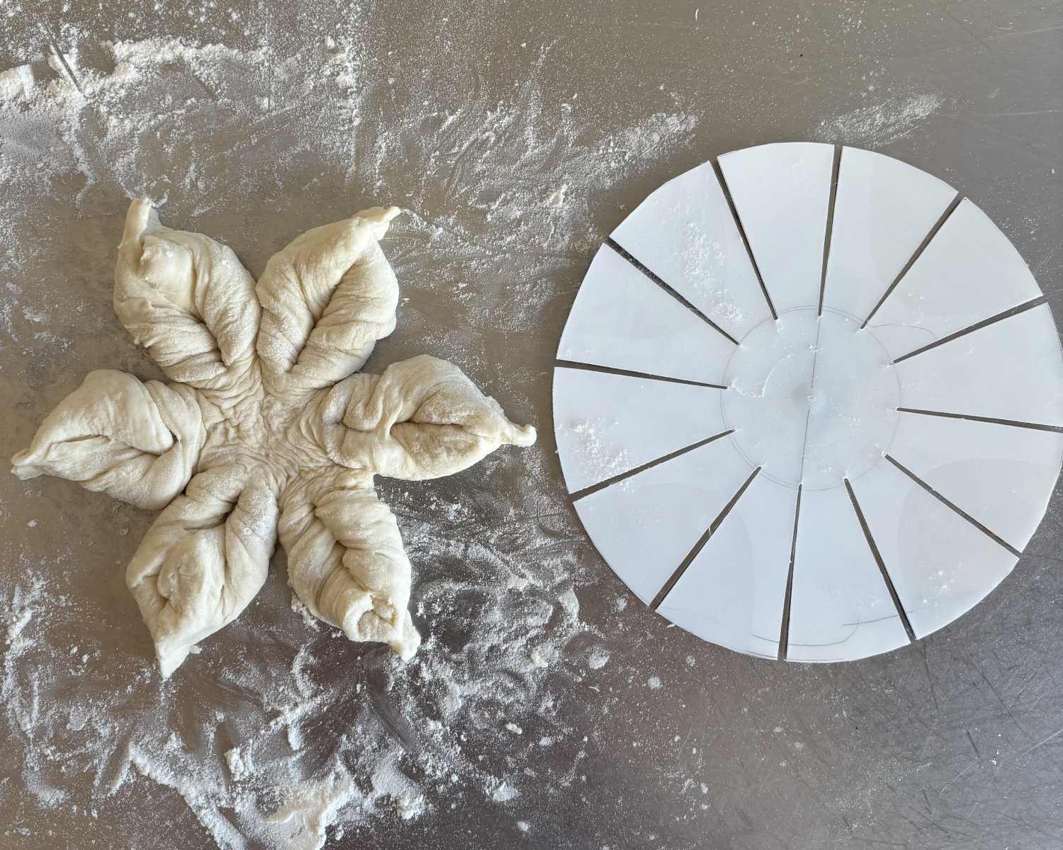 A piece of star bread dough sits next to a circular plastic dough divider on a floured metal surface.