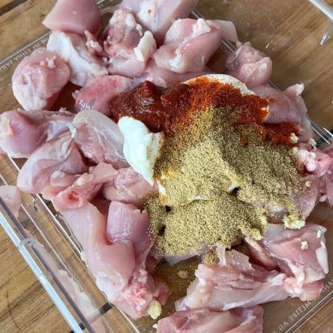 Raw cubed chicken, yogurt and spices in a glass dish