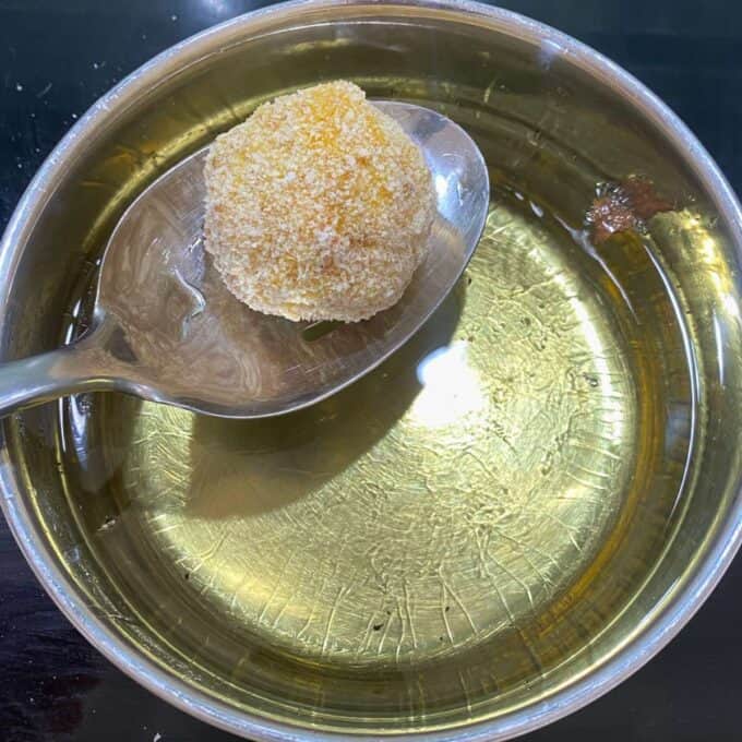 A rolled and coated in flour arancini ball filled with mozzarella about to be put into a pot of hot oil