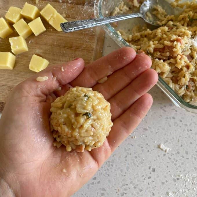A hand forming a arancini ball with a cube of mozzarella in the middle