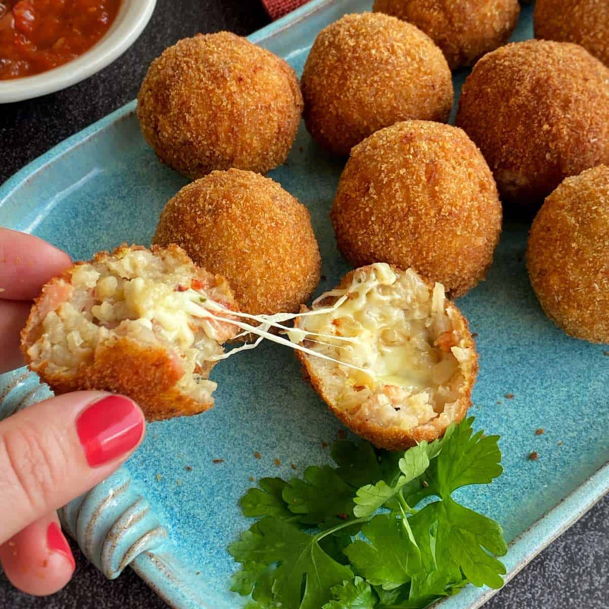 A hand pulling opening a arancini ball filled with mozzarella