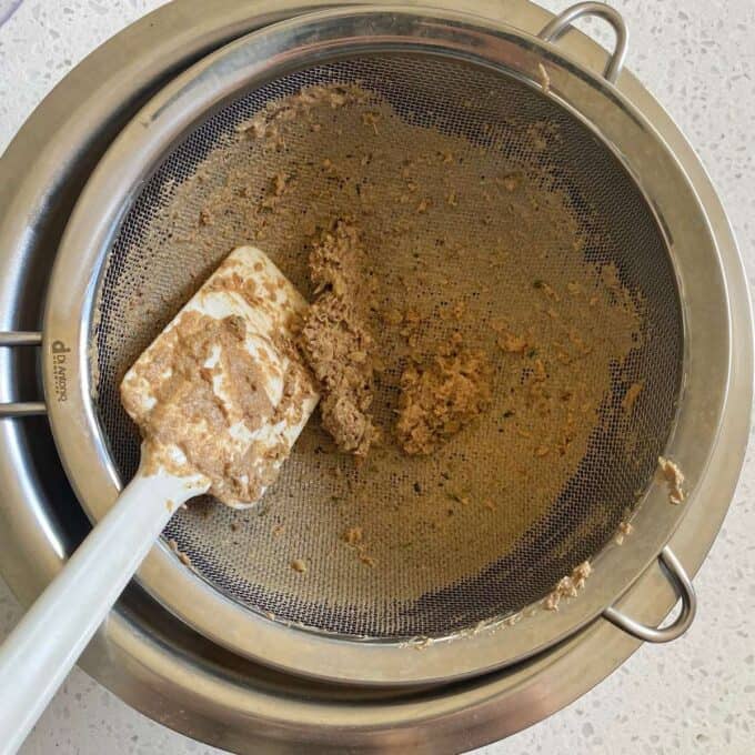 Cooked and blended chicken livers being pushed through a sieve to make smooth