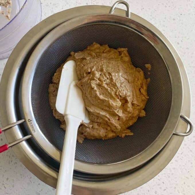 Cooked and blended chicken livers being pushed through a sieve to make smooth