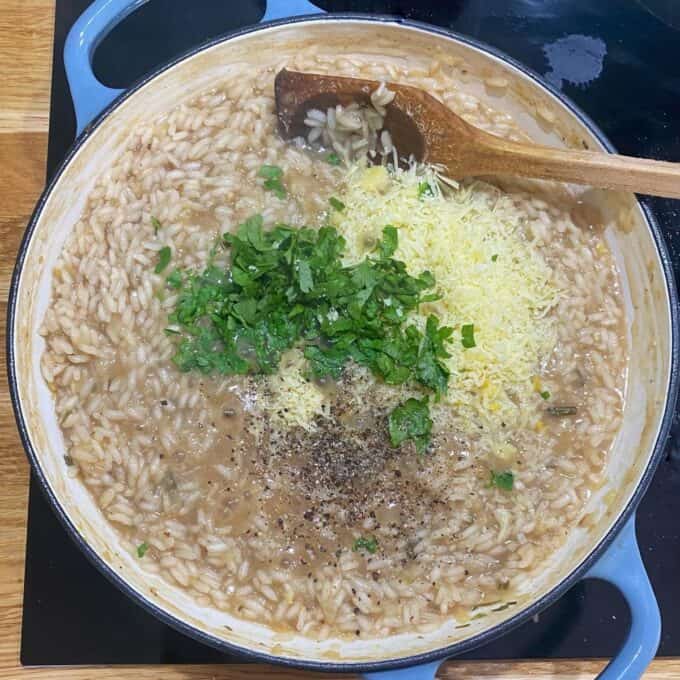 Herbs, parmesan and spices being added to the risotto in a round ceramic dish
