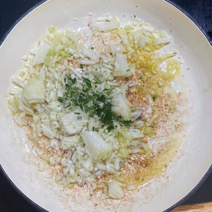 Cubed onion and spices frying in a round ceramic dish