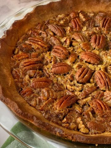 A close up shot of a cooked pecan pie on a glass plate