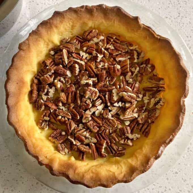 A cooked pie crust with roasted pecan's inside on a glass cake stand
