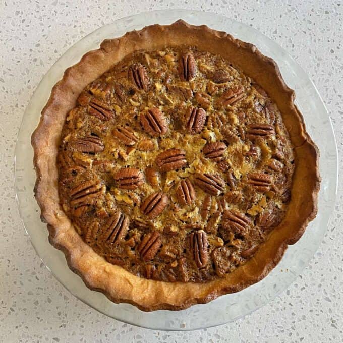 A birds eye view shot of a cooked pecan pie on a round glass cake stand