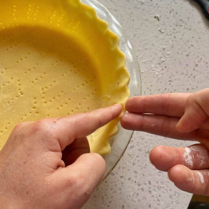 Fingers gently pressing pastry into a pie dish to form the edge