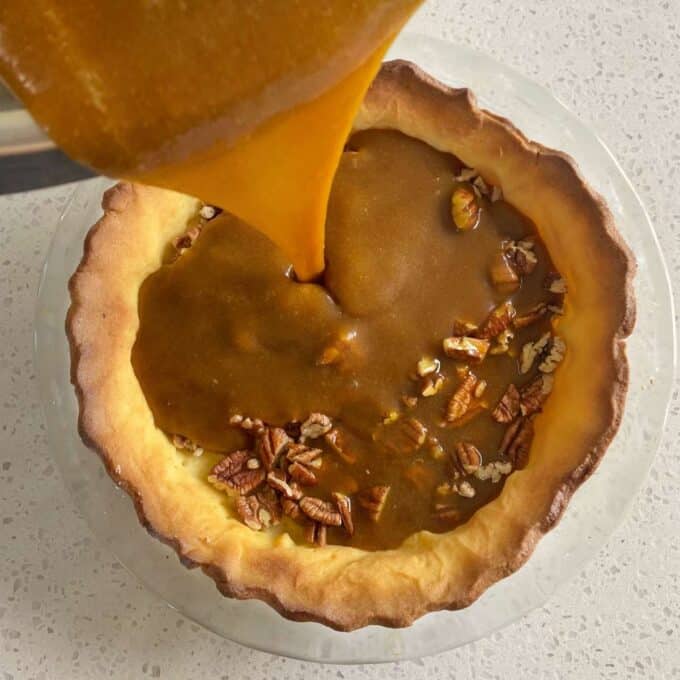 Cooked through brown sugar and butter being poured into the cooked pie crust with pecans inside to form the pecan pie filling