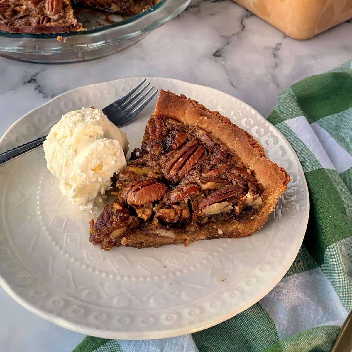 A slice of cooked pecan pie served with a scoop of vanilla ice cream on a small white plate