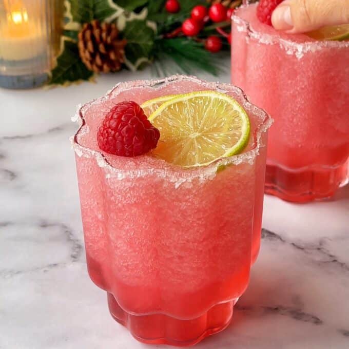 Two cranberry margaritas served with a slice of lime and a raspberry