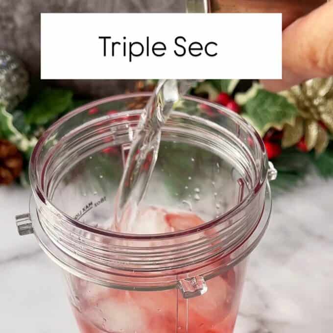 Triple sec being added to the cranberry margarita mixture in a Ninja cup.