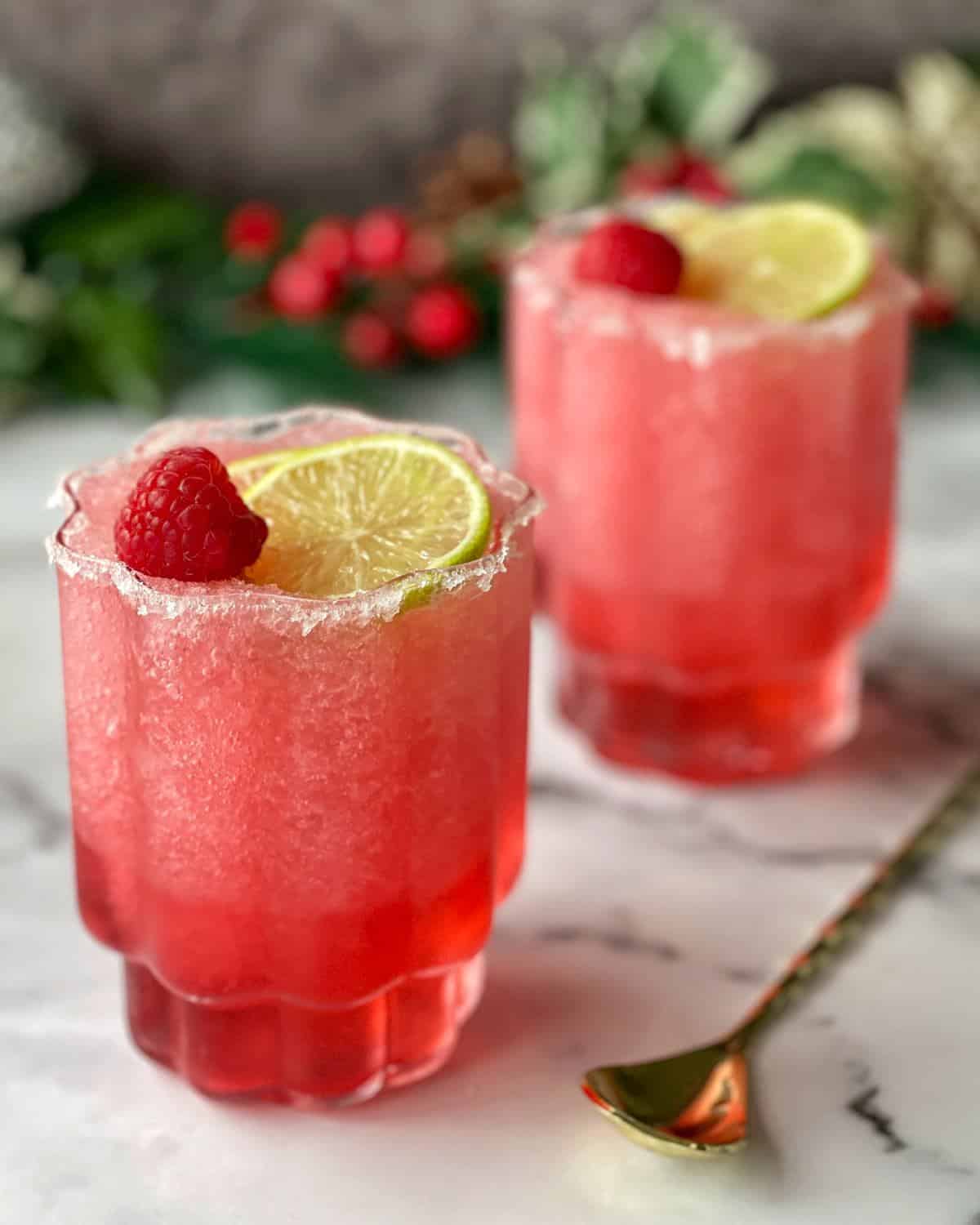 Frozen Cranberry Margarita Two cranberry margaritas served with a slice of lime and a raspberry