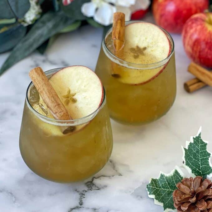Two Winter Wonderland Cider's served with a cinnamon stick and a slice of fresh apple on a marble bench top