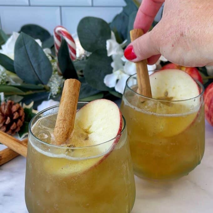 Two Winter Wonderland Cider's served with a cinnamon stick and a slice of fresh apple on a marble bench top