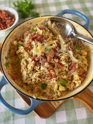 BIrd's eye view of a ham and parmesan risotto in a blue serving dish on a green gingham table cloth.