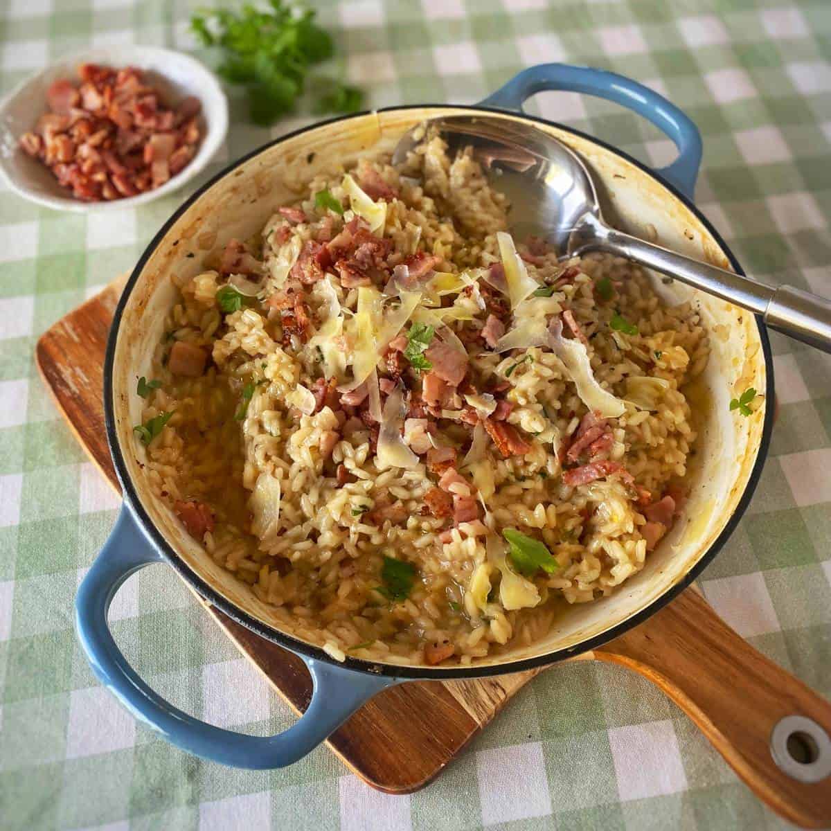 BIrd's eye view of a ham and parmesan risotto in a blue serving dish on a green gingham table cloth.