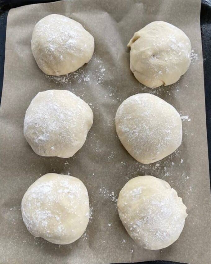 6 balls of floured dough on a lined baking tray.
