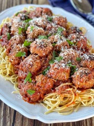 A plate of spaghetti topped with meatballs and tomato sauce, garnished with grated cheese and parsley, on a wooden table.