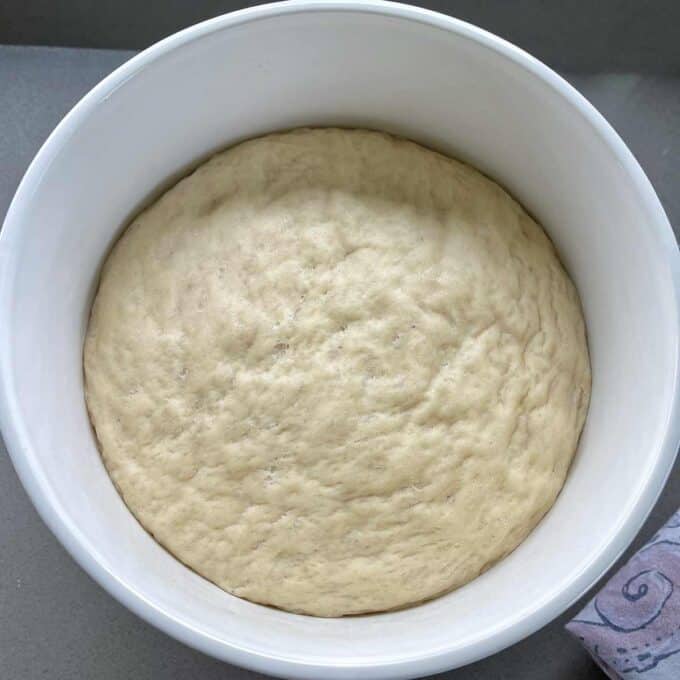 A white bowl containing risen bread dough, resting on a gray surface.