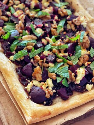 A close up of a beetroot and feta and walnut tart on a wooden chopping board.