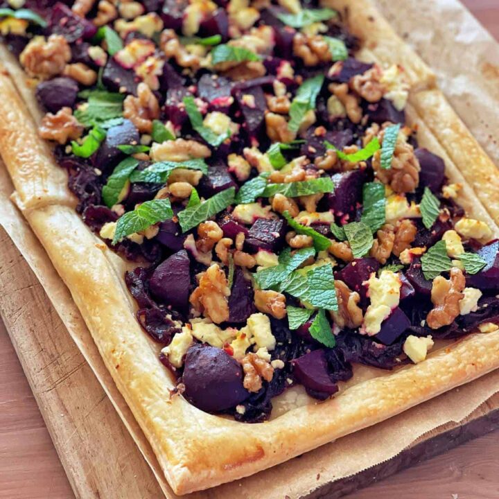 A close up of a beetroot and feta and walnut tart on a wooden chopping board.