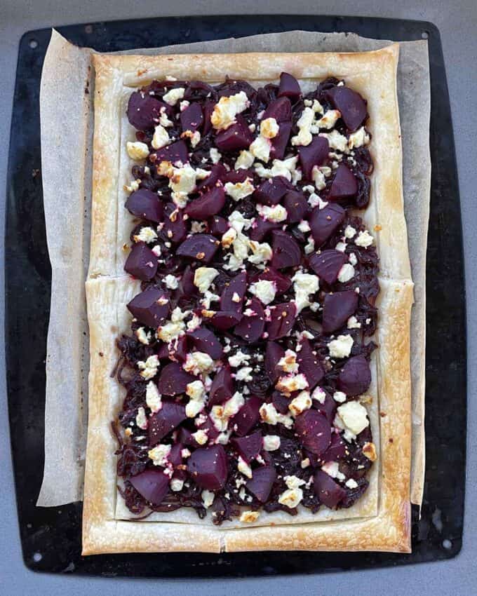A cooked beetroot and feta tart on a lined baking tray.