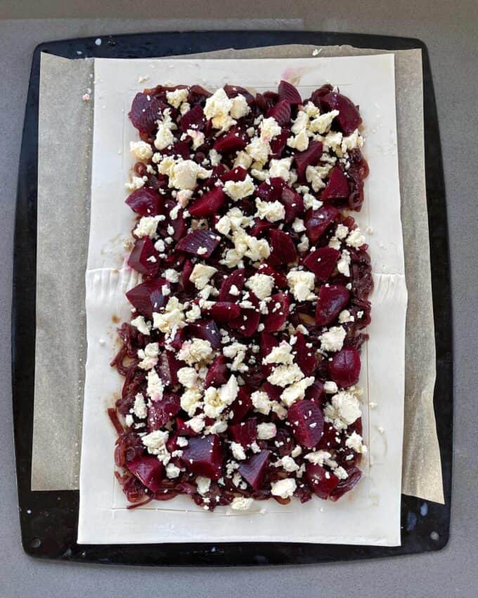 Beetroot and feta on a piece of uncooked puff pastry on a lined baking tray.