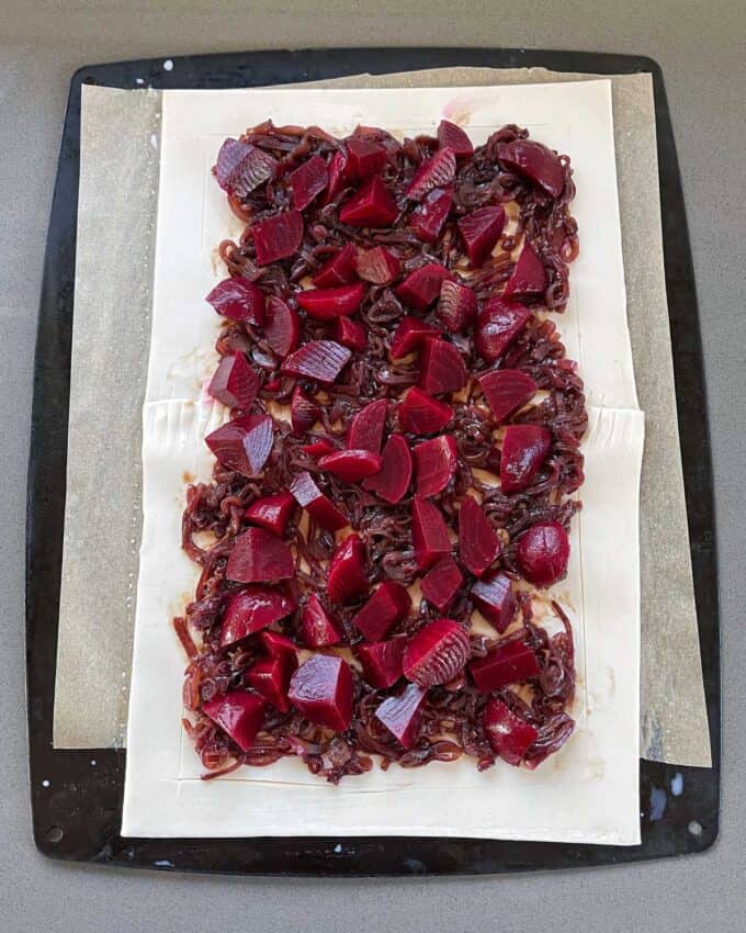 Caramelised onion and beetroot on a piece of uncooked puff pastry on a lined baking tray.
