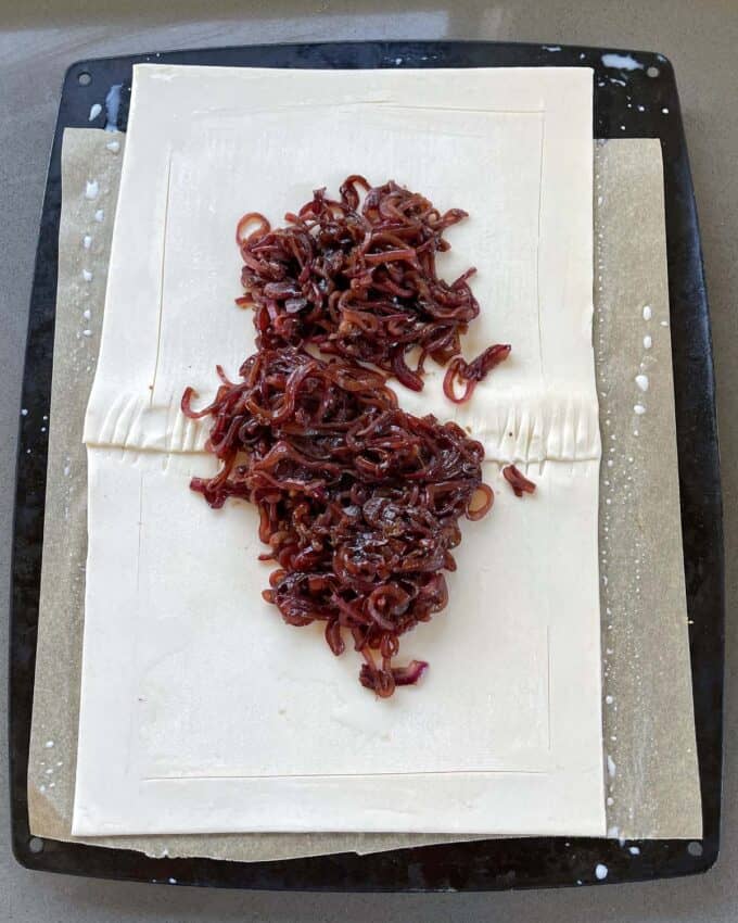 Caramelised onion on two pieces of puff pastry on a lined baking tray.