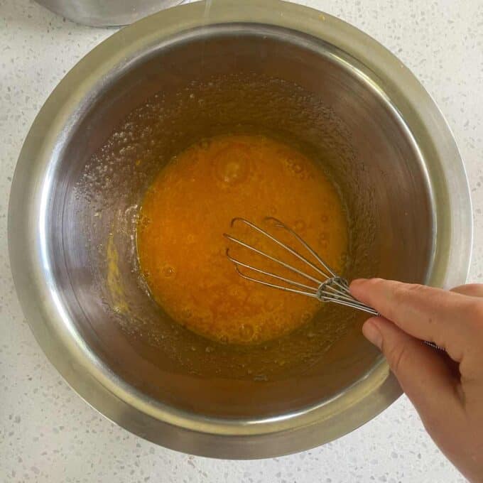 A hand whisking orange mixture in a metal bowl.