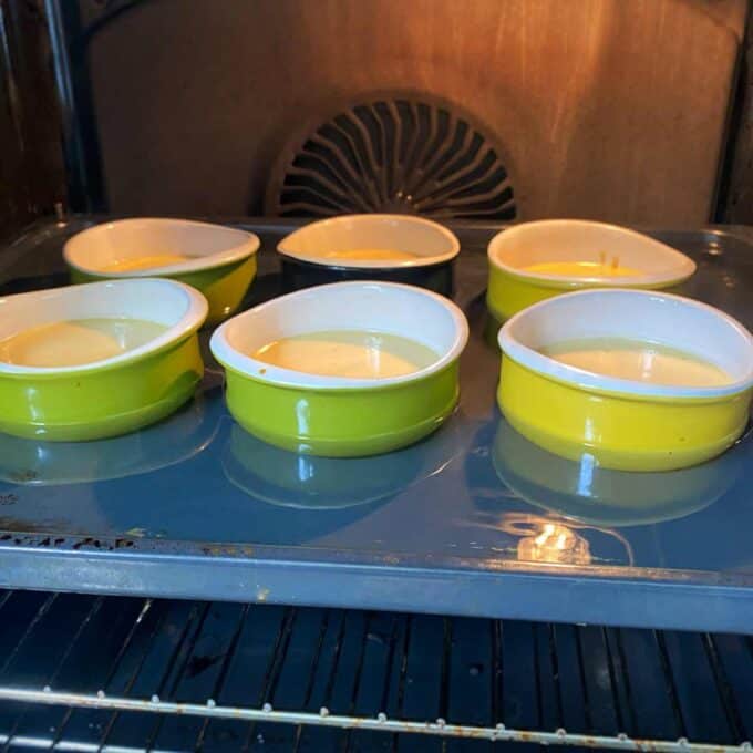 Six ramekins filled with batter, three green and three yellow, sit on a tray inside an oven.