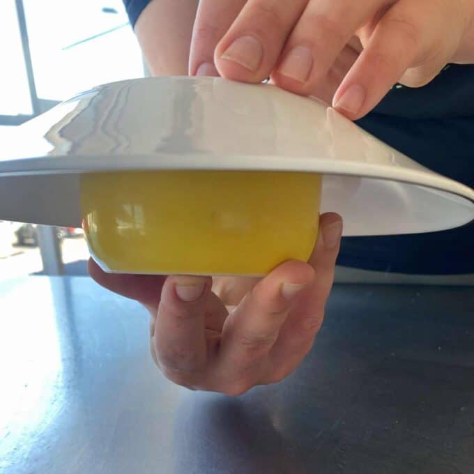 Hands lifting a white plate with a yellow cylindrical object underneath.